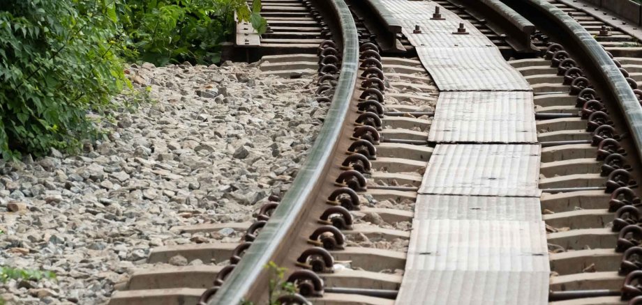 Ein kurviges Bahngleis schlängelt sich durch eine grüne, bewachsene Umgebung. Die Schienen beschädigt – ein Hinweis auf Hitzeeinwirkung oder strukturelle Instabilität.
