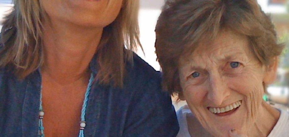 Zwei Frauen sitzen lachend nebeneinander und strahlen Lebensfreude aus. Das Wort „Demenz“ steht oben im Bild – es vermittelt Nähe, Verständnis und Menschlichkeit im Umgang mit Demenzbetroffenen.