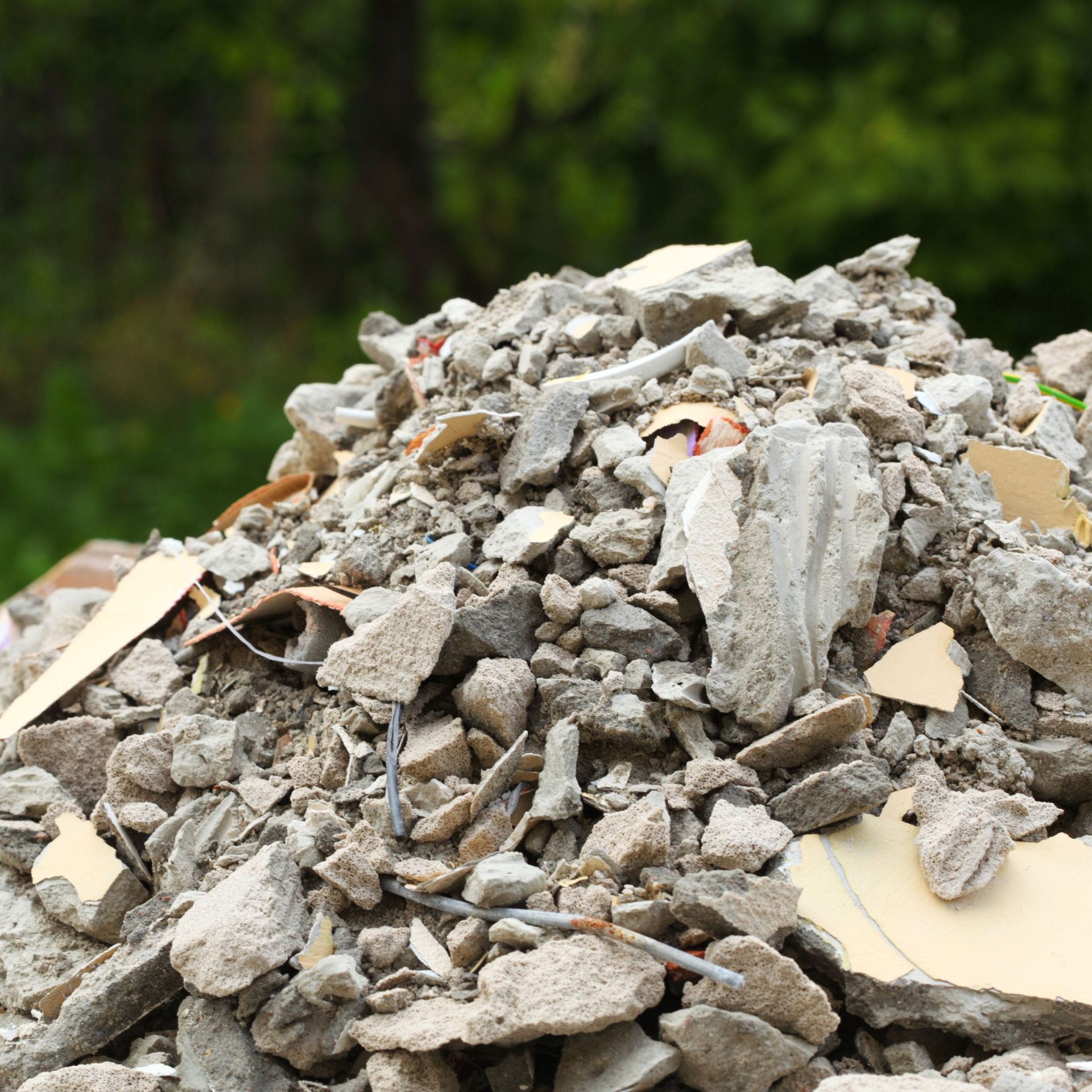 Ein Haufen aus Bauschutt, Betonresten und zerbrochenem Material liegt im Freien. Zwischen den Trümmern sind Kabel und Putzstücke zu sehen – ein Beispiel illegaler Müllablagerung in der Natur.
