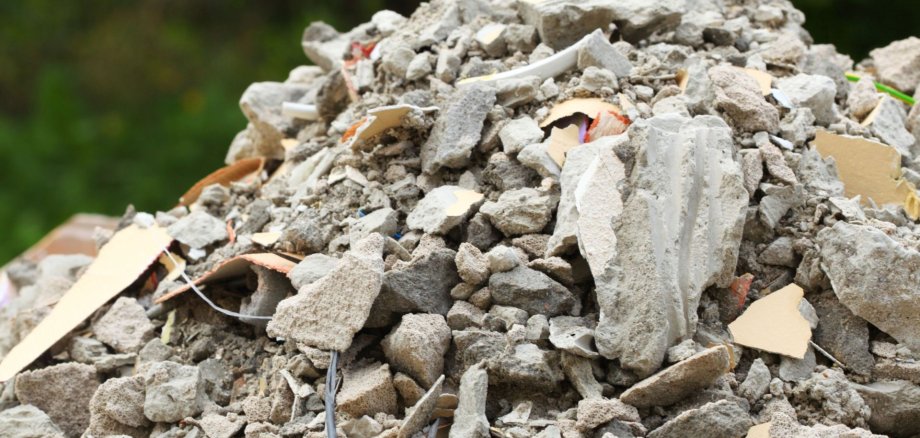 Ein Haufen aus Bauschutt, Betonresten und zerbrochenem Material liegt im Freien. Zwischen den Trümmern sind Kabel und Putzstücke zu sehen – ein Beispiel illegaler Müllablagerung in der Natur.