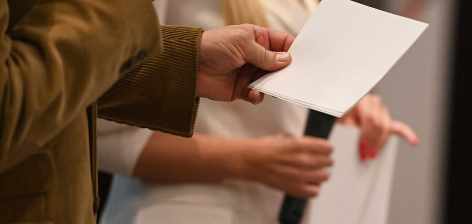 Zwei Personen stehen auf einer Bühne und halten Mikrofone sowie Moderationskarten in den Händen. Die Szene wirkt professionell – typisch für eine Veranstaltung, Präsentation oder Preisverleihung.