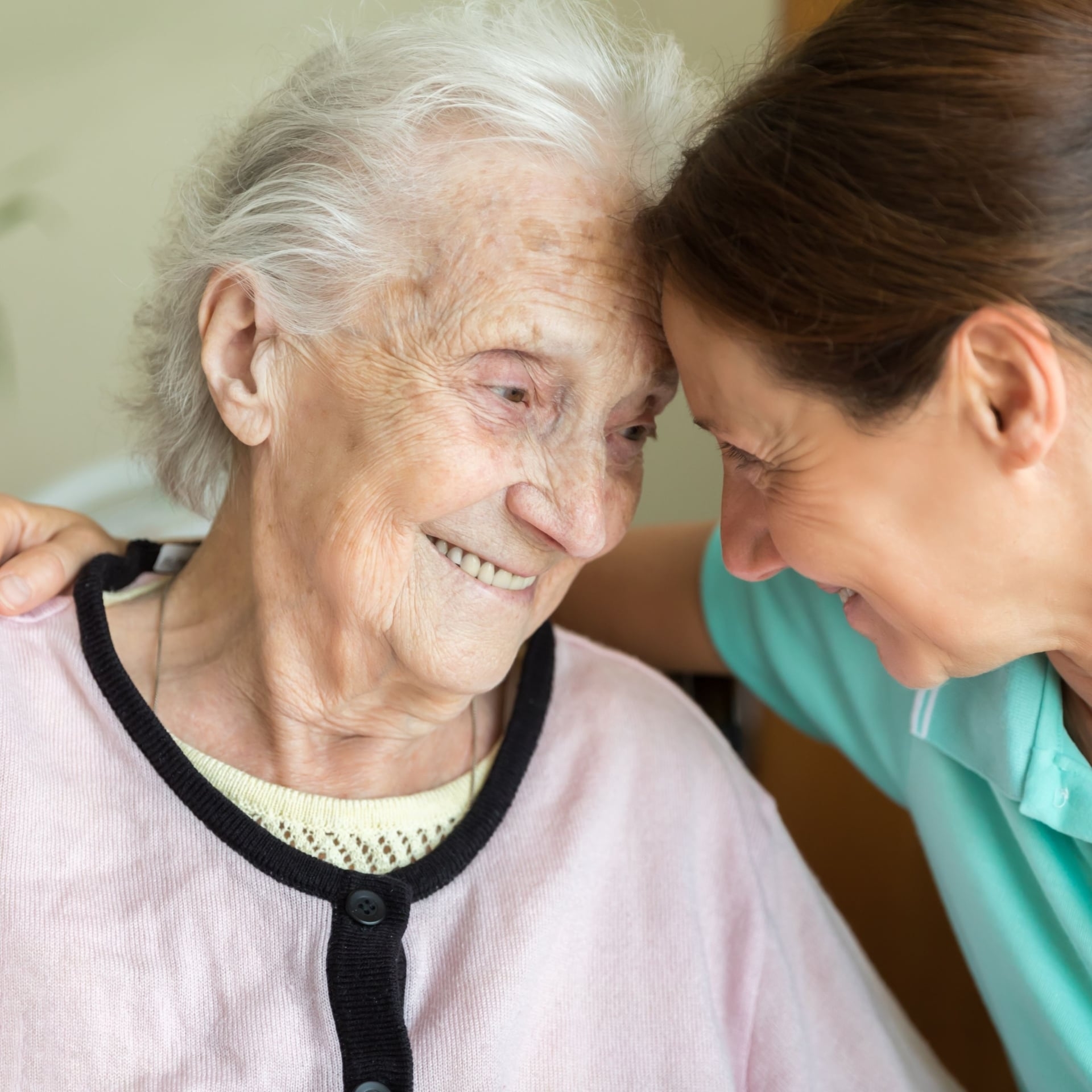 Eine Pflegerin und eine ältere Frau lächeln sich liebevoll an und berühren ihre Stirnen. Das Bild vermittelt Nähe, Vertrauen und Herzlichkeit – ein Moment menschlicher Zuwendung in der Pflege.