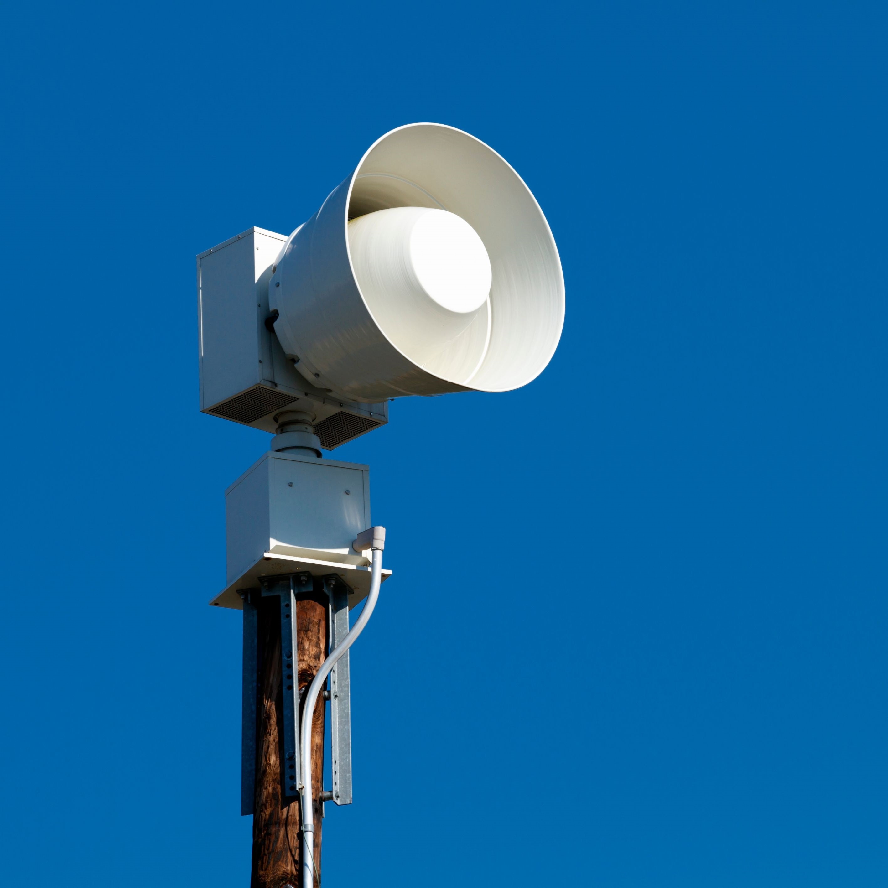 Eine moderne Sirene ist auf einem Mast montiert und ragt vor einem klaren blauen Himmel empor. Das Bild symbolisiert Katastrophenschutz, Warnsysteme und die Bedeutung öffentlicher Sicherheitsinfrastruktur.
