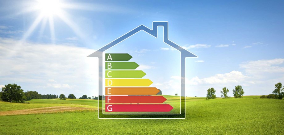 Ein schematischer Hausumriss mit einem Energielabel (A-G) steht auf einer weiten grünen Wiese unter blauem Himmel mit strahlender Sonne. Es symbolisiert Energieeffizienz und umweltfreundliches Wohnen.