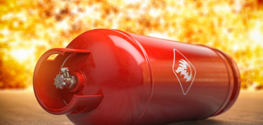 Eine rote Gasflasche mit einem Flammen-Warnsymbol liegt auf dem Boden. Im Hintergrund ist eine Explosion zu sehen, was auf Gefahr hinweist.